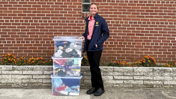 Female student stands next too three full boxes of donated clothing. 