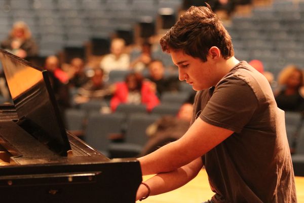 Young man playing a grand piano on stage. 