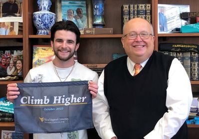 Timothy Reidell holds a blue flag with the phrase "Climb Higher" next to campus president Chris Gilmer, Ph.D.