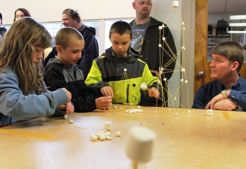 Children attending last year’s Mineral County STEM Festival were challenged to build the tallest tower out of spaghetti straws that would support the largest marshmallow. Lending some advice is Brandon Felton, far right, a mechanical engineer with RK&K Ci
